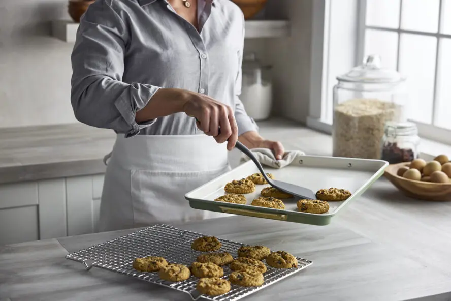 Image of a woman taking fresh cookies off of a GreenPan Reserve sheet pan in Sage Green.