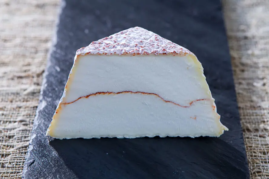 Image of a pyramid of goat cheese from Capriole Farm cut in half, with a vein of paprika running through the middle.