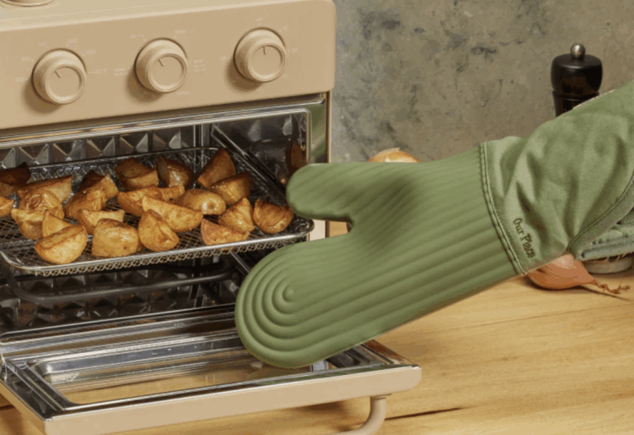 Image of an Our Place Hot Mitt in the color sage being used to remove a tray of roasted potatoes from an air fryer oven.