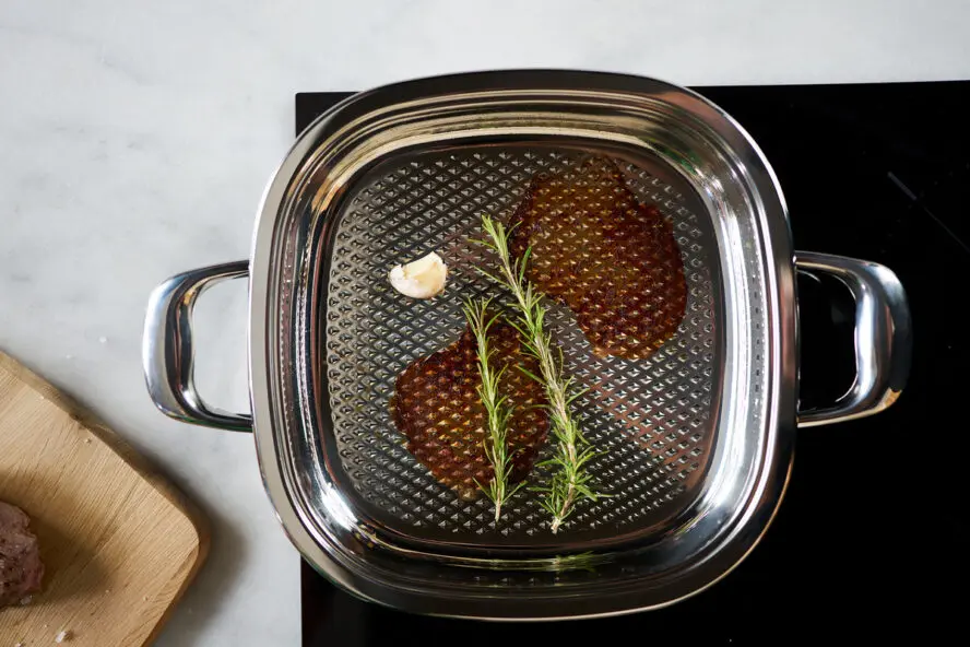 Image of the AbyAMC grill pan shown on a stovetop, where you can see marks where steaks were seared.
