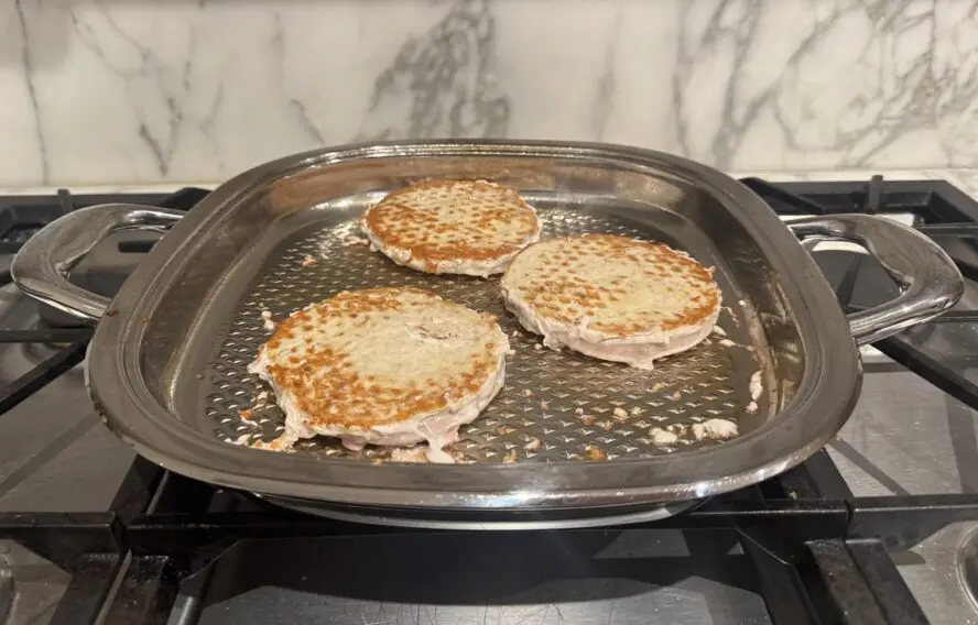 Image of three turkey burgers being seared on the AbyAMC stovetop grill pan with lid.