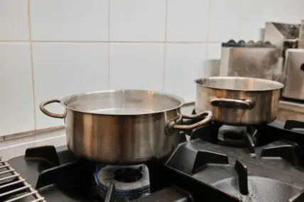 Image of an old pot on a stovetop with a stack of pots and pans beside it.