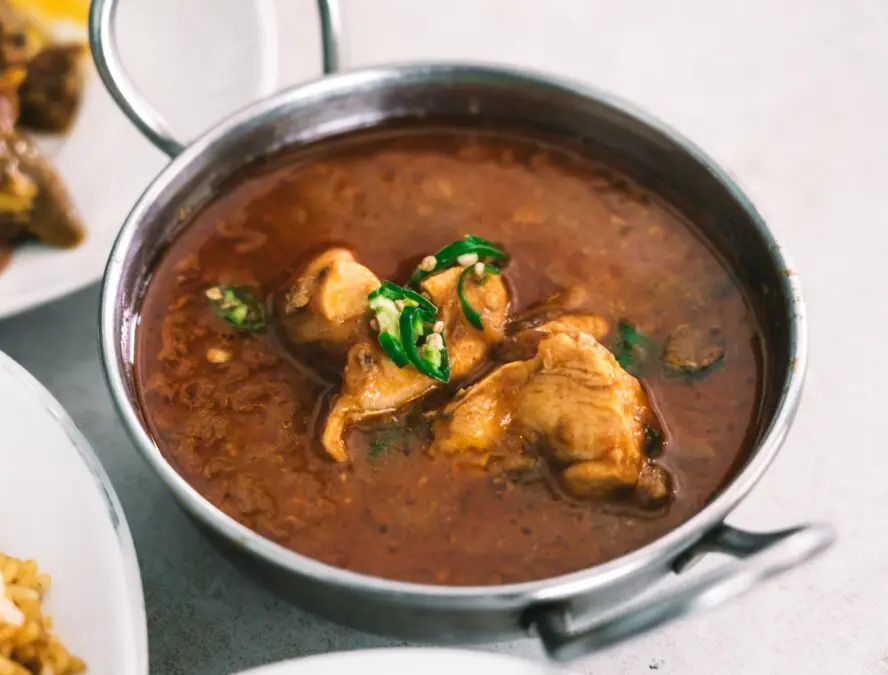 Image of a kadai filled with a chicken curry set on a table.