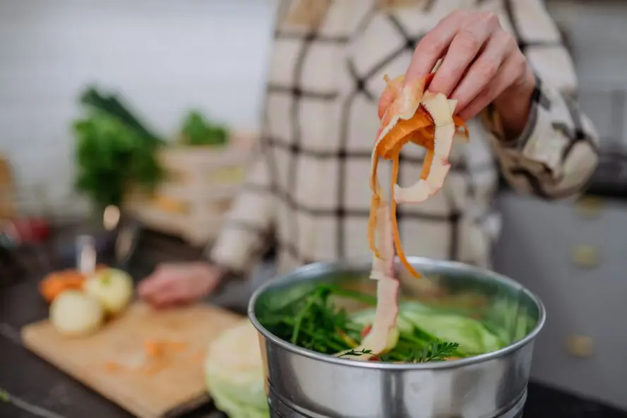 Image of a woman putting some onion skin into a large stock pot full of other bits of vegetables.