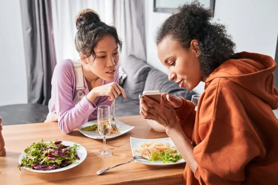 Image of two women sitting at a dining table, chatting and looking at a phone screen.