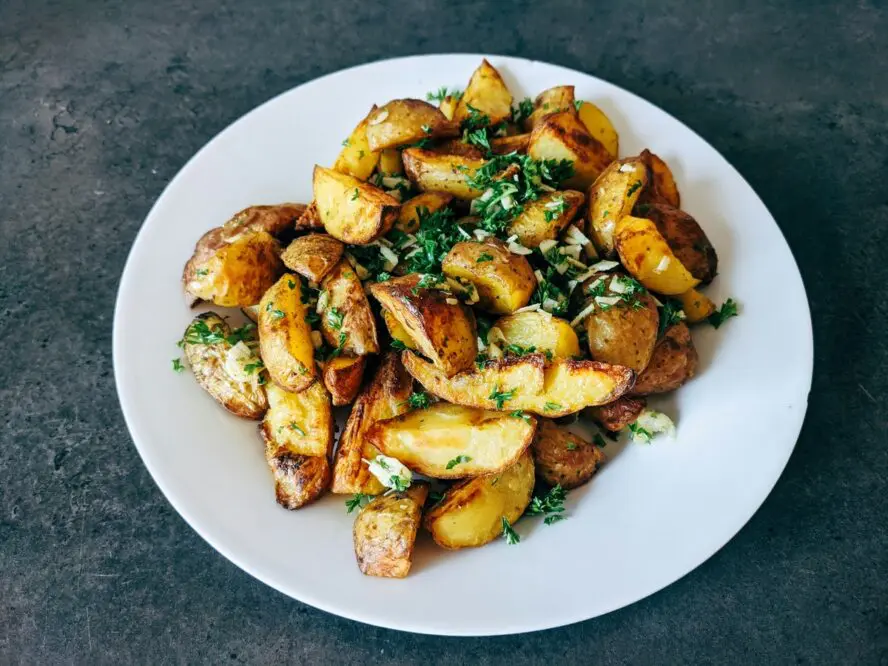 Image of a plate of crispy roasted potatoes with tossed with garlic and parsley.
