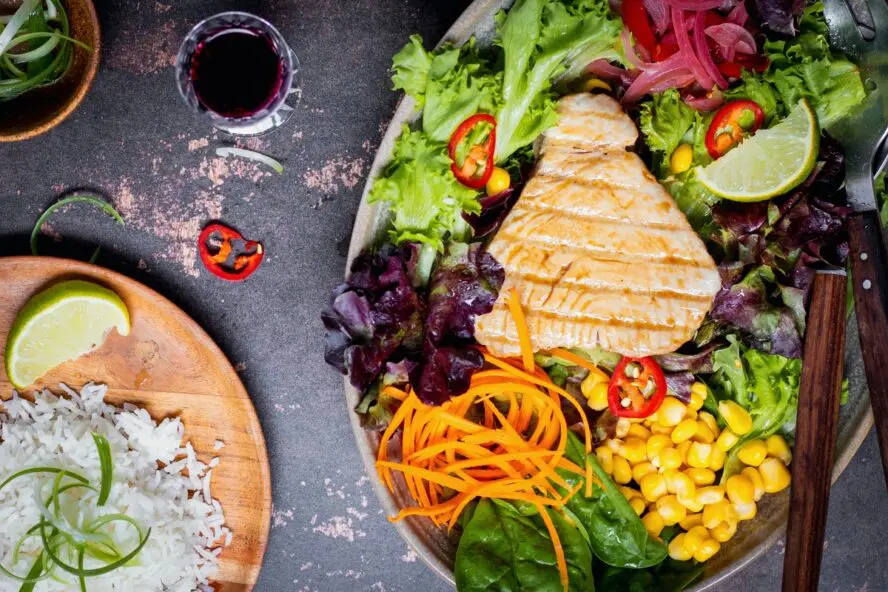 Image of a fresh salad topped with a lean protein with grill marks.