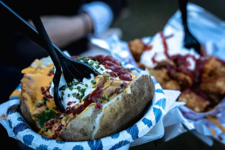 Image of someone digging into a baked potato with all the trimmings, sour cream, bacon, and cheese.