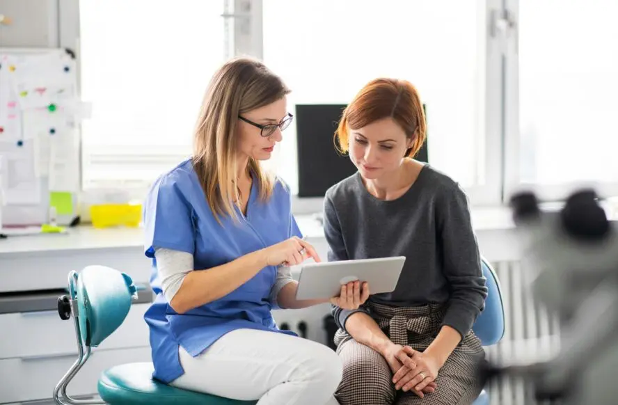 Image of a woman with red hair sitting next to a physician, looking at an iPad together.