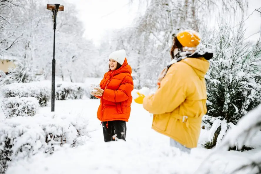 Image of two women wearing colorful puffer jackets standing in a snowy winterscape.