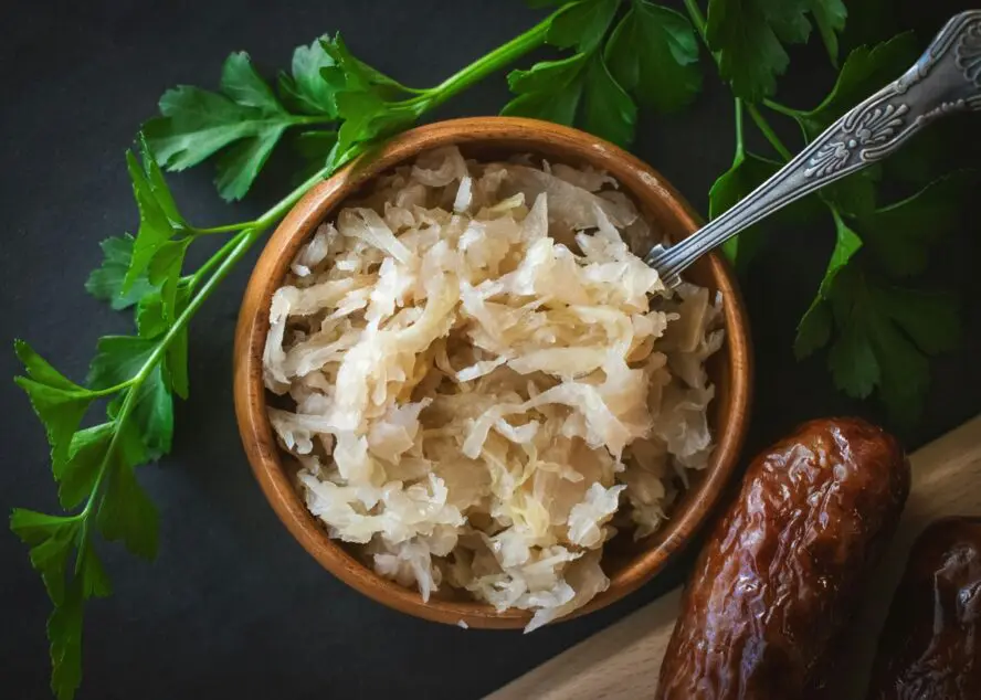 Image of a small bowl of sauerkraut with a spoon inside the bowl, on a black table.