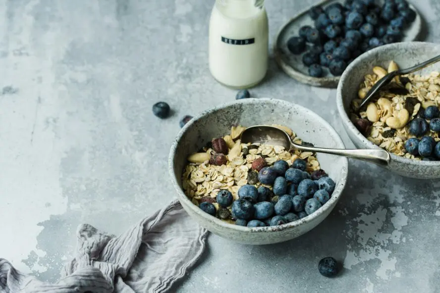 Image of a bowl full of dry oats and blueberries, set next to a bottle of Kefir.