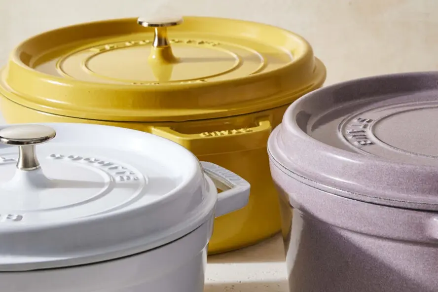 Image of three Staub round cast iron Dutch ovens in a soft white, yellow, and purple.