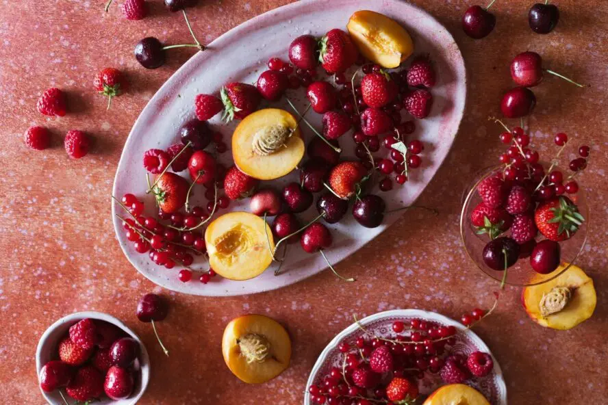 Image of a gorgeous dish full of cherries, strawberries, raspberries, and peaches against a pink background.