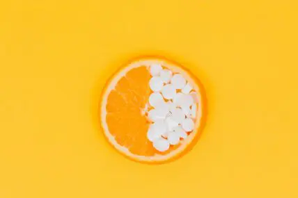 Image of a slice of orange laid flat, with half of the fruit replaced with small white supplement pills.