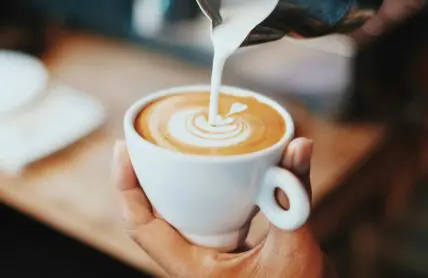 Image of a barista pouring steamed milk into a coffee cup to create latte art.