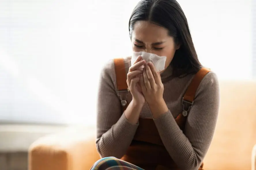 Image of a young woman blowing her nose into a tissue.