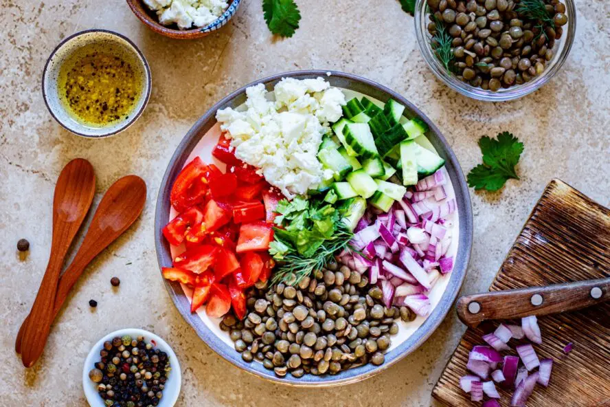 Image of a large salad with peppers, feta, cucumbers, onions, and beans (lentils) in a bowl.