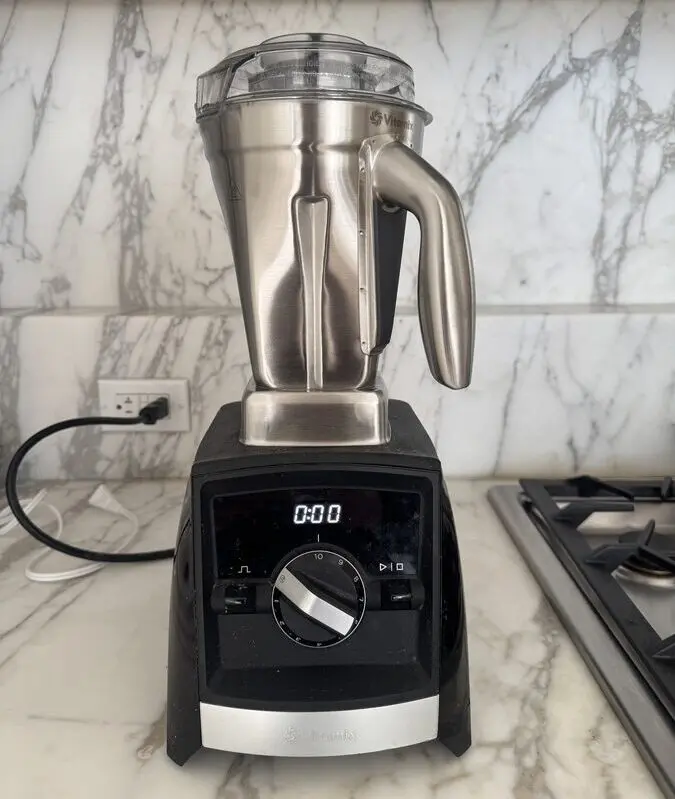 Image of the Vitamix Stainless Steel blender jar on a Vitamix base, on a marble countertop.