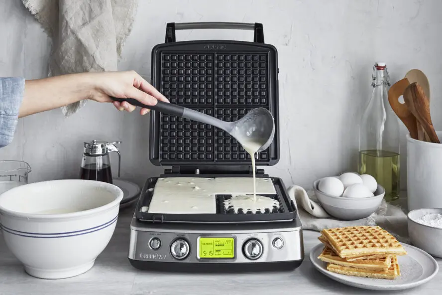 Image of the GreenPan Elite Ceramic Nonstick 4-Square Waffle Maker, with a hand pouring batter into the plates.