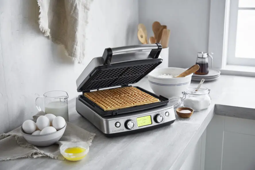 Image of the GreenPan Elite Ceramic Nonstick 4-square Waffle Maker with a bowl of eggs and maple syrup next to it.