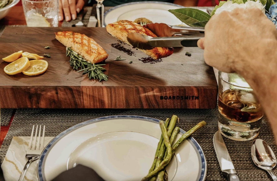 Image of a Boardsmith Walnut board being used as a serving platter for salmon fillets on a dining table.