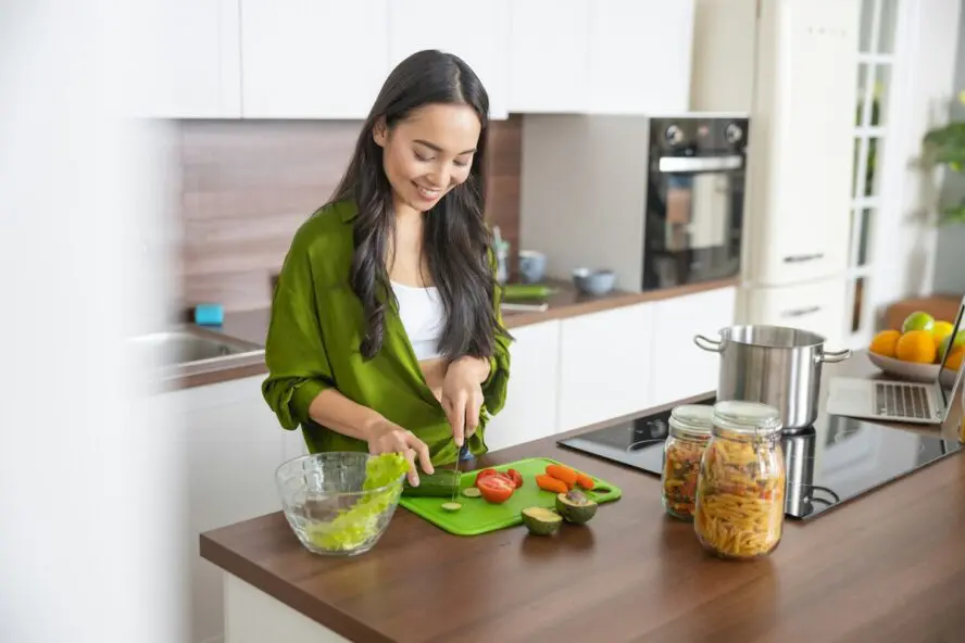 Image of a young woman cutting vegetables on a green plastic cutting board.