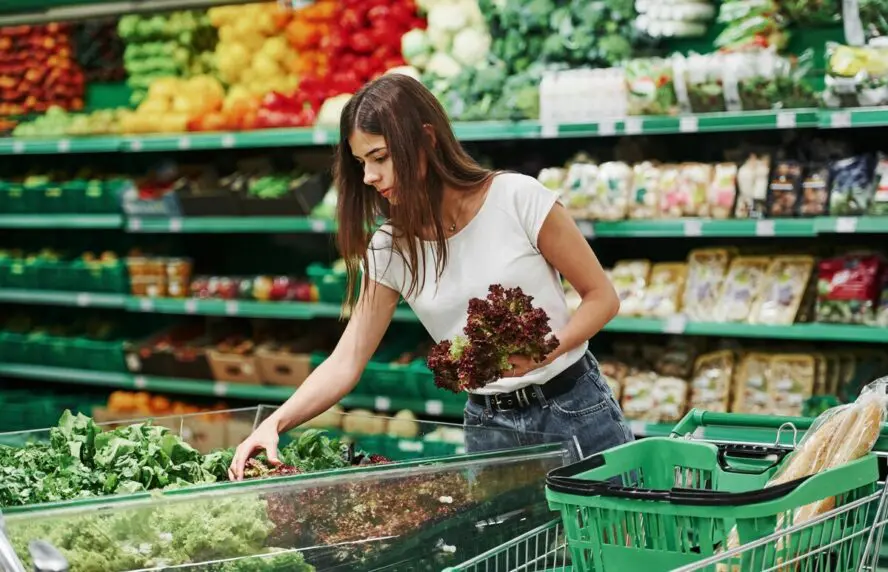 Image of a young woman picking up produce items in a supermarket.