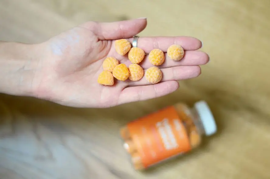 Image of an open palm with a handful of orange gummy vitamins, floating above the bottle.