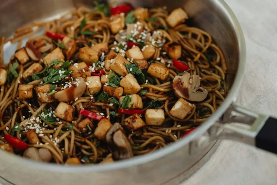 Image of a large stainless steel pan filled with stir-fried soy sauce noodles, tofu, and vegetables.
