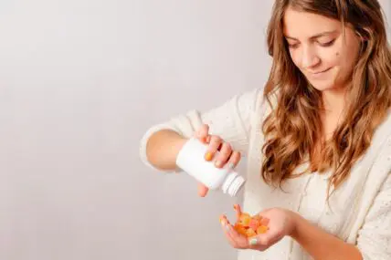 Image of a young woman pouring a bottle of gummy vitamins into her hand.