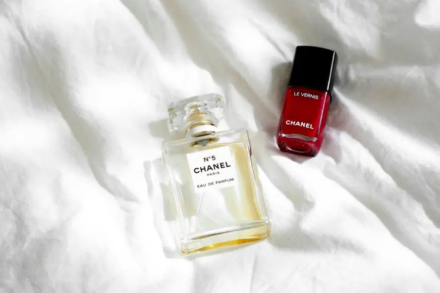 Image of a bottle of Chanel No. 5 perfume and a red nail polish set against a white silk background.