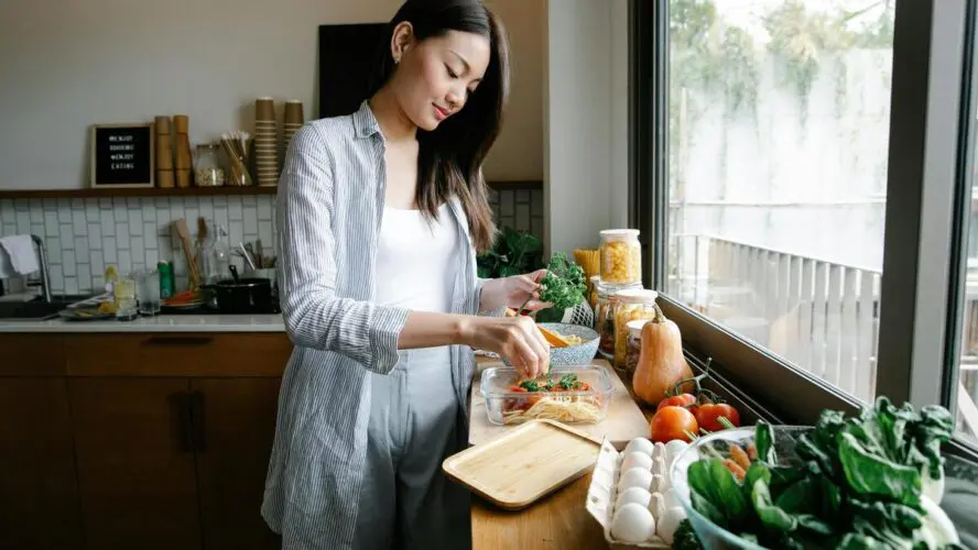 Image of a young woman standing in a kitchen preparing a meal with fresh ingredients.
