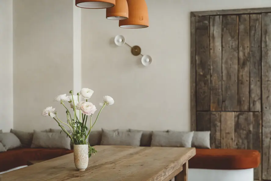 Image of a rustic tablescape from HOY Hotel with a vase of white flowers against lots of pale wood.