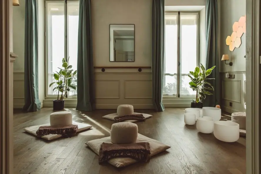 Image of a calming room with tall windows, pillows on the floor, and sound bowls at the front of the room.