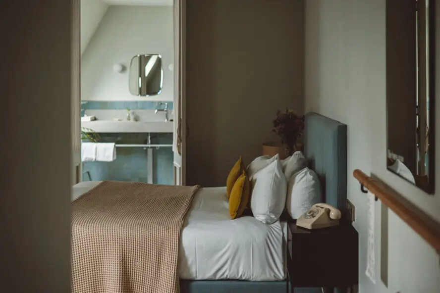 Image of a cool-toned, relaxing bedroom in HOY Hotel, with a view of the bathroom beyond the bedroom.