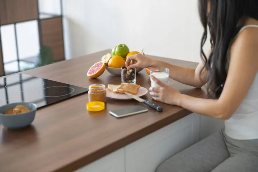 Image of a young woman enjoying her breakfast at a table with a glass of milk and peanut butter on toast.