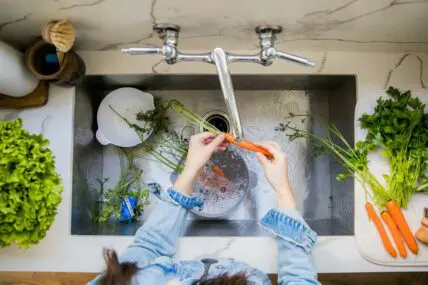 Overhead shot of a sink with a pair of hands washing a small pile of carrots under running water.