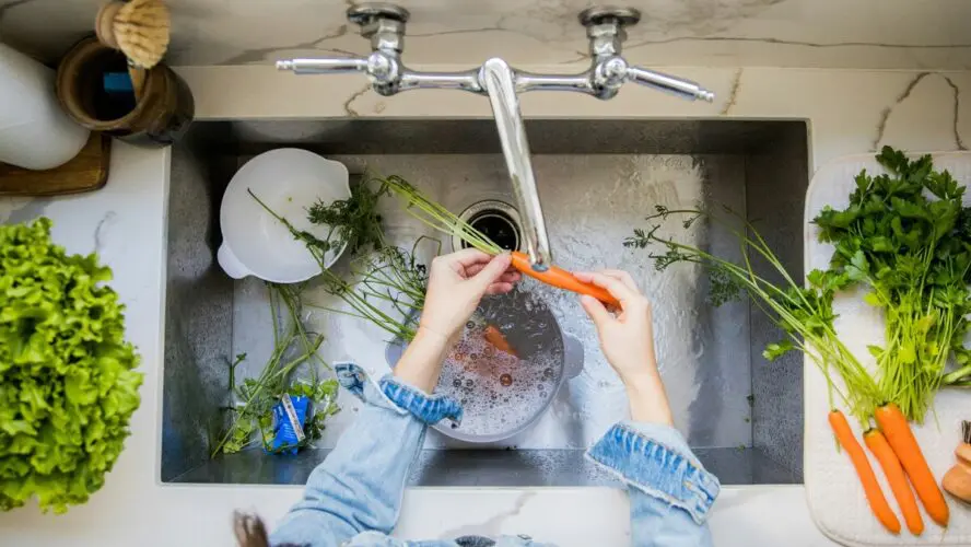 Overhead shot of a sink with a pair of hands washing a small pile of carrots under running water.