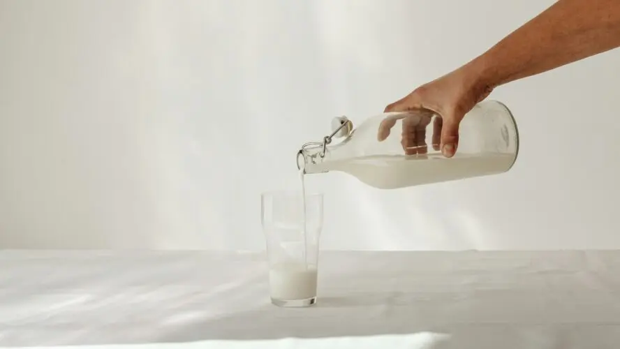 Image of a hand pouring milk into a glass from a bottle.