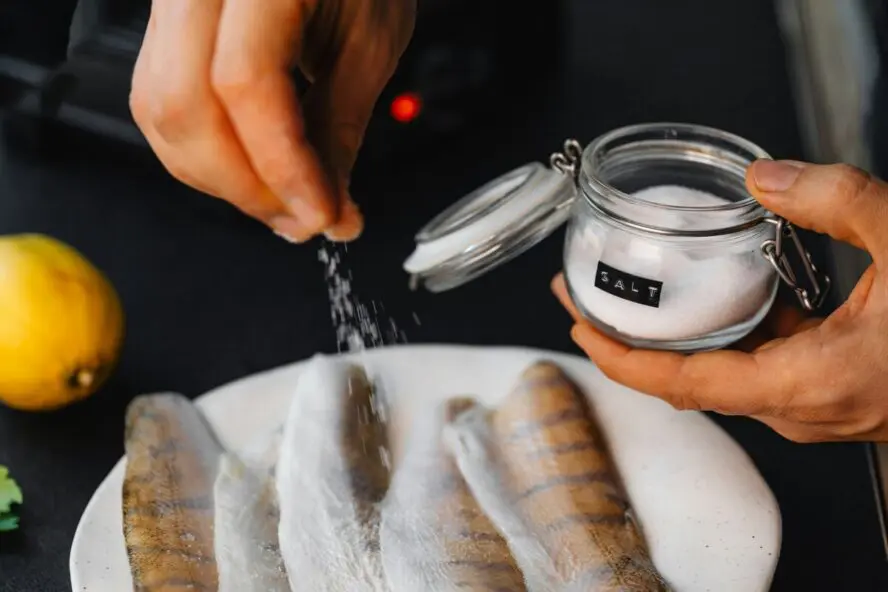 Image of a hand sprinkling salt over a plate of fish.