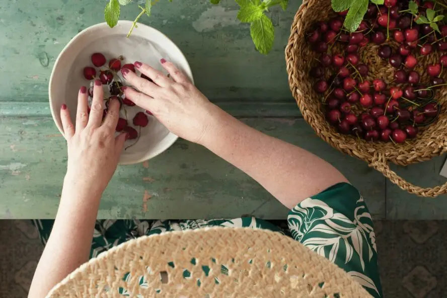 Overhead image of a woman soaking cherries in a bowl of vinegar.