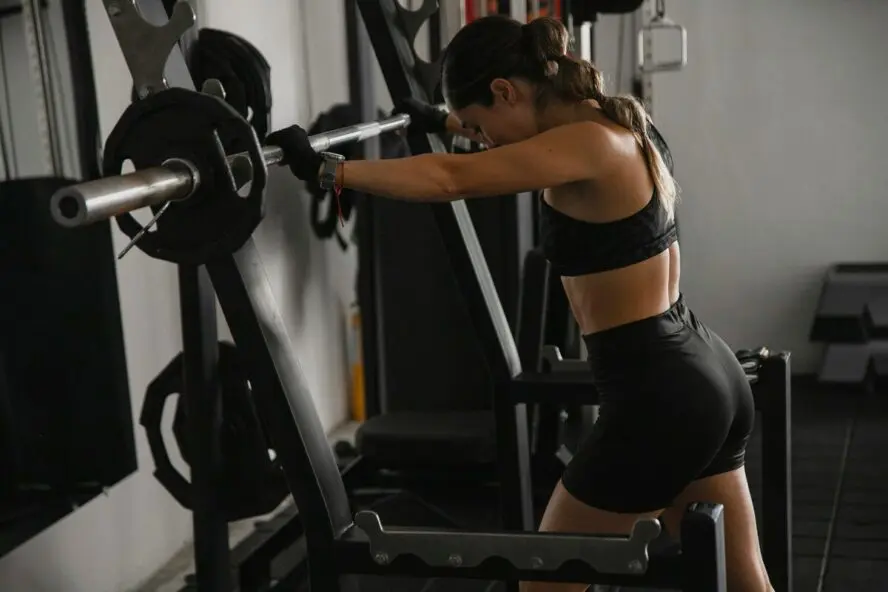 Image of a young woman wearing sportswear in a gym and leaning against a rack with a barbell.