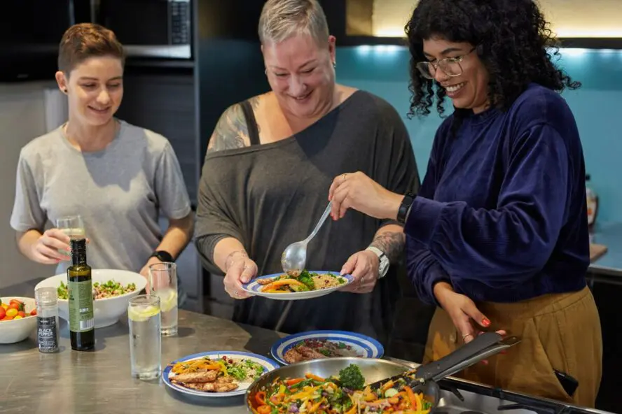 Image of three women serving dinner in a kitchen and enjoying their evening together.