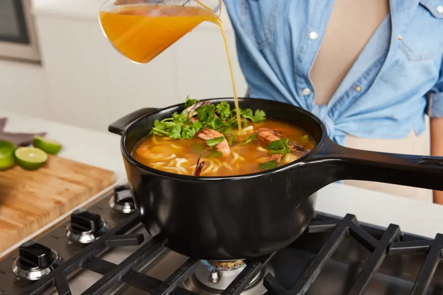 Image of a woman pouring broth into a large Xtrema saucepan on the stove.
