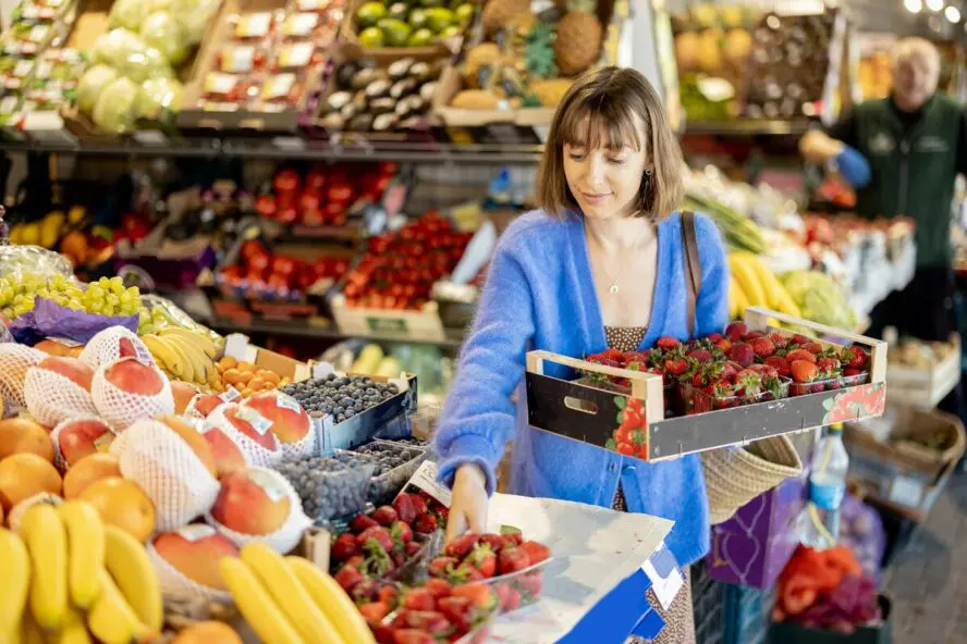 Image of a young woman at a farmer's market, selecting strawberries and putting them in a large crate.