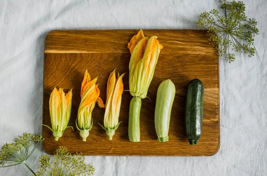 Image of several summer squash and zucchini blossoms shown on a wooden cutting board.