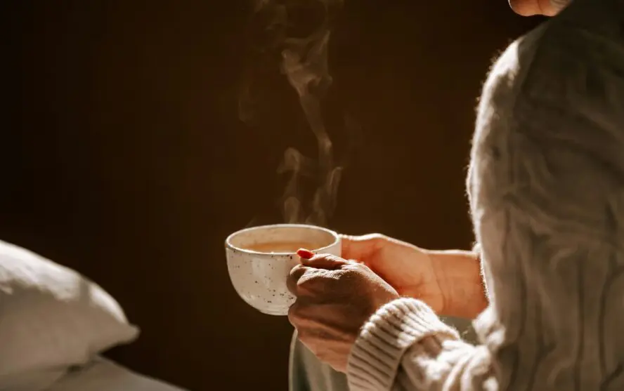 Image of a woman holding a cup full of steaming hot coffee or tea.