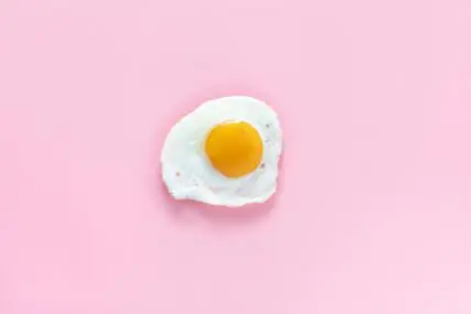 Image of a fried, single sunny side up egg shown on a solid pink background.