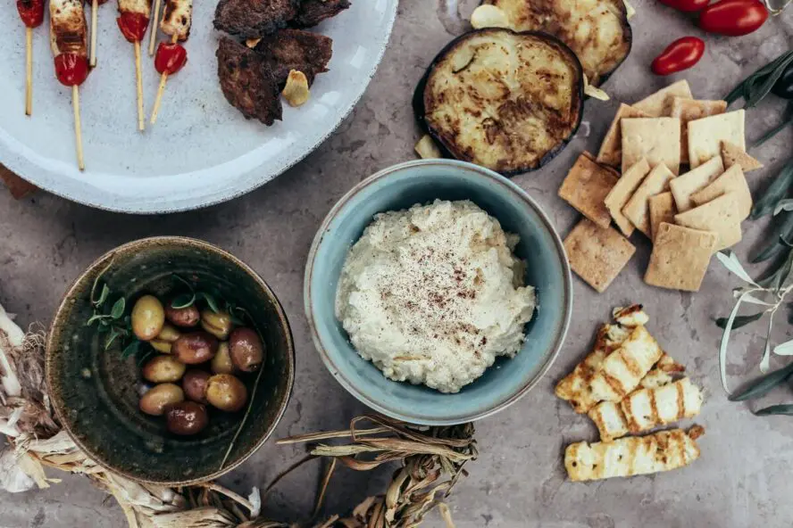 Image of a large spread of Mediterranean foods, including olives and a cup of seasoned cottage cheese.